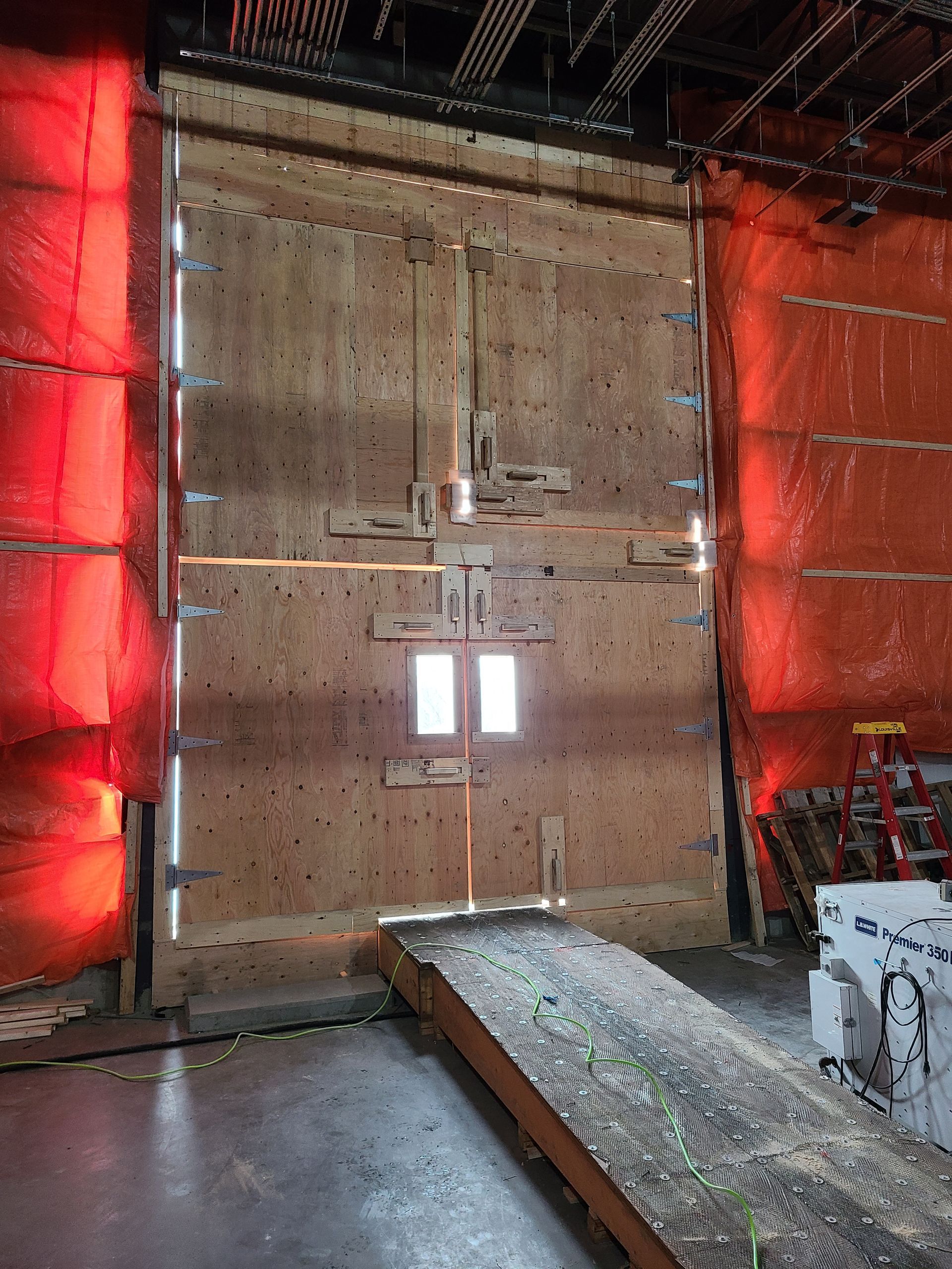 Grande porte en bois avec une petite fenêtre, rampe d'accès, à l'intérieur d'un espace industriel.