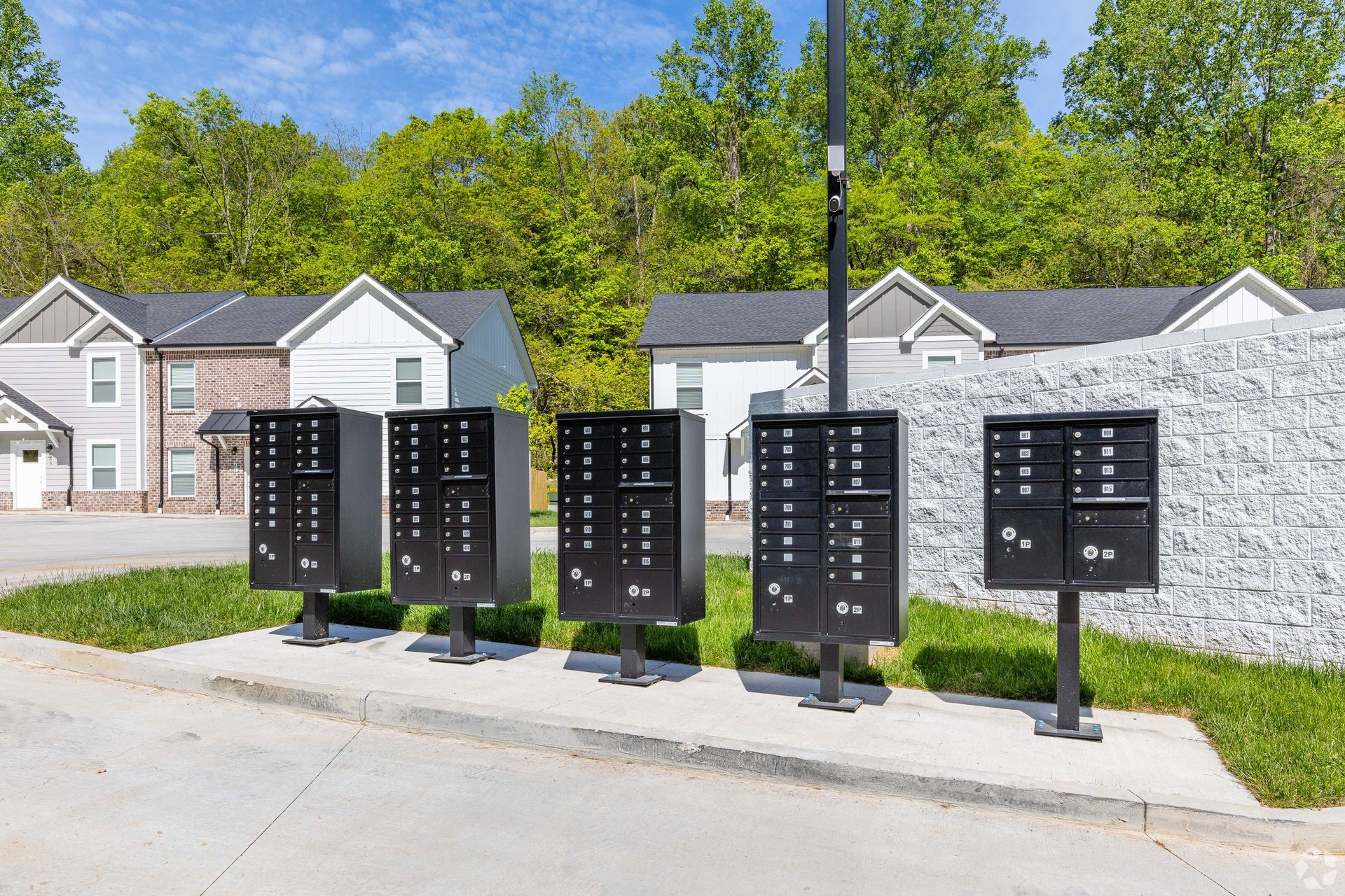 Five black mailboxes on stands near a residential area.