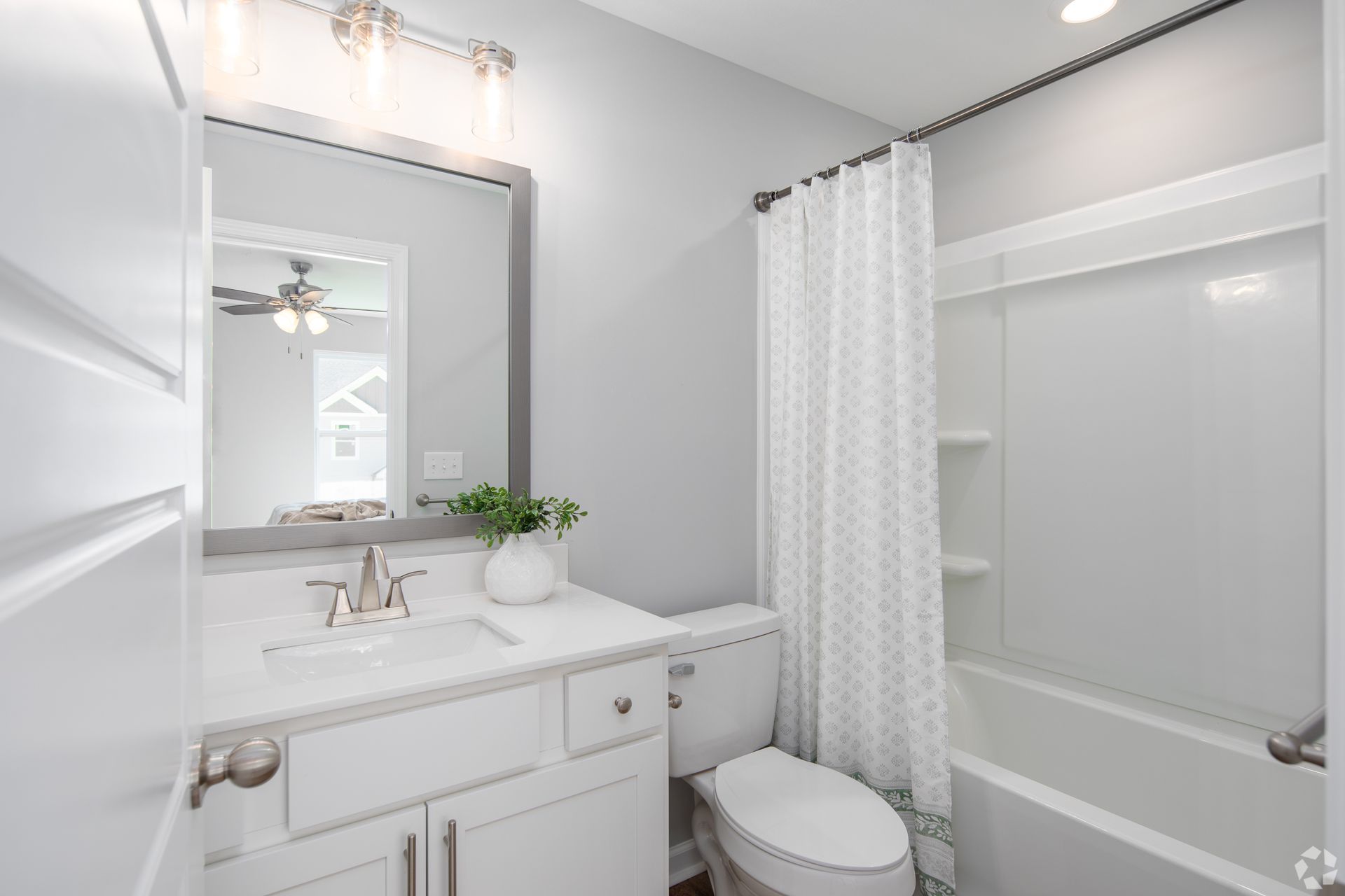 White bathroom with sink, toilet, and bathtub. Light gray walls and white shower curtain.