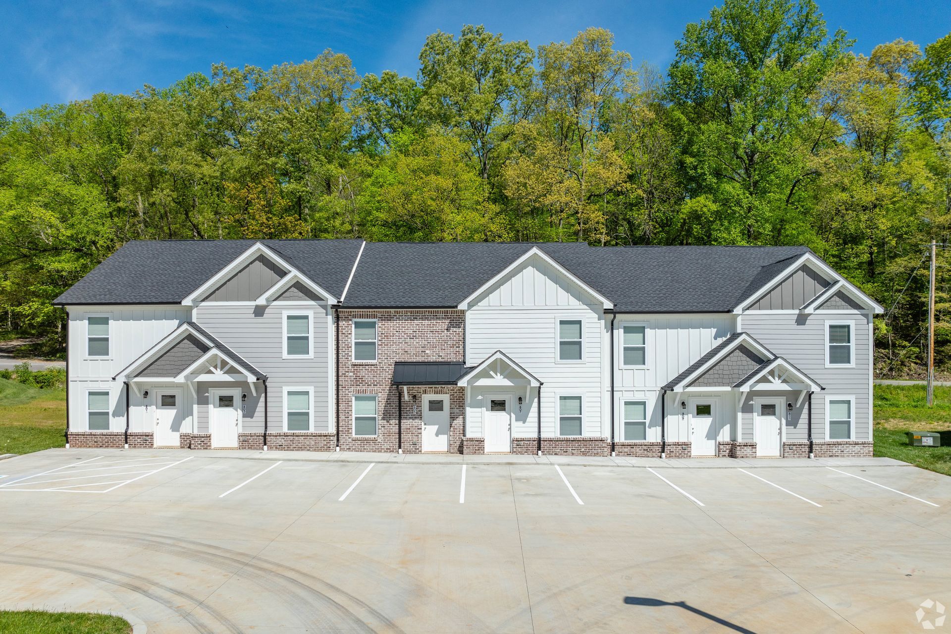 Row of modern townhouses with light gray siding, brick accents, and a paved parking lot.