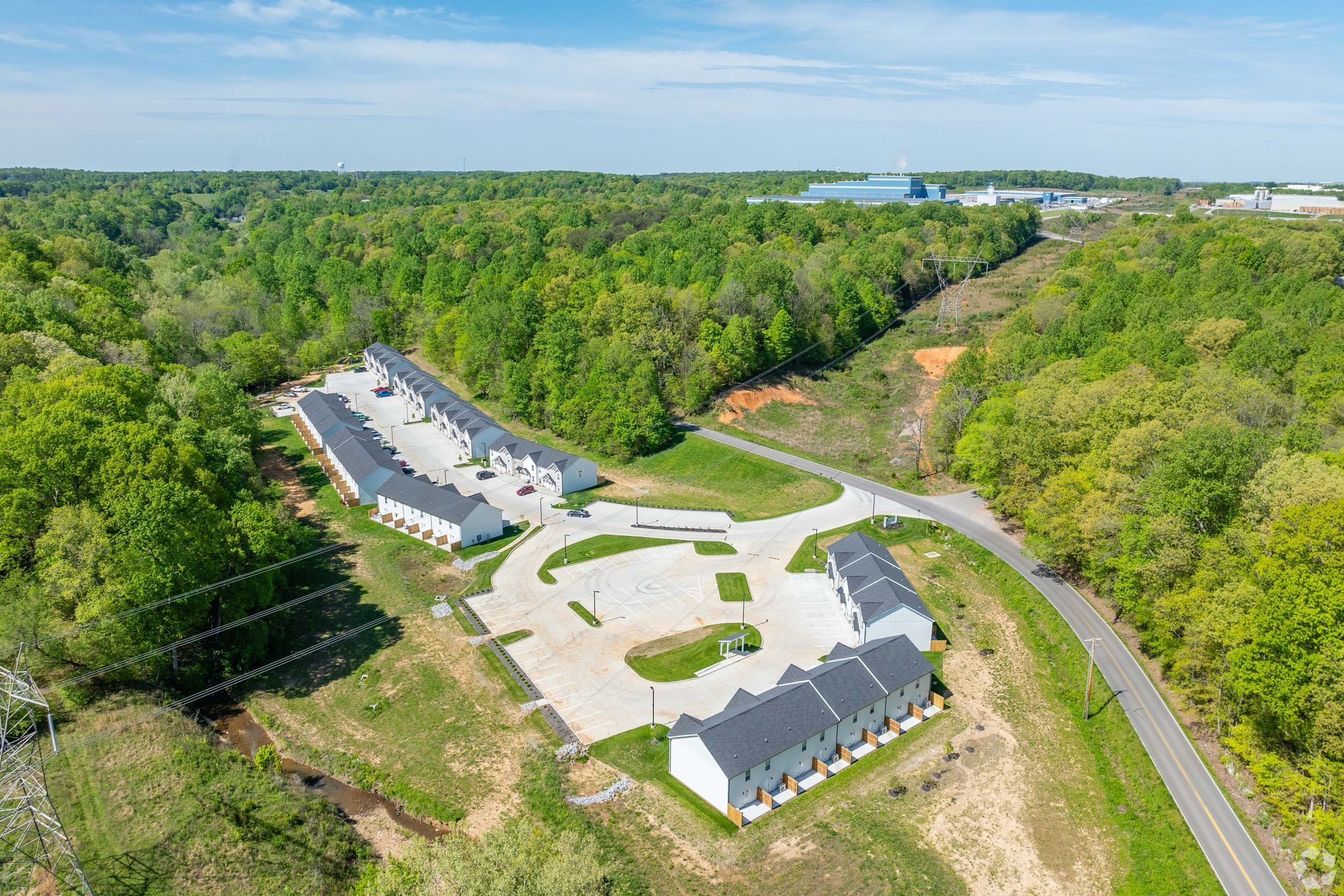 Aerial view of townhomes with white exteriors, asphalt driveways, and surrounding green trees.