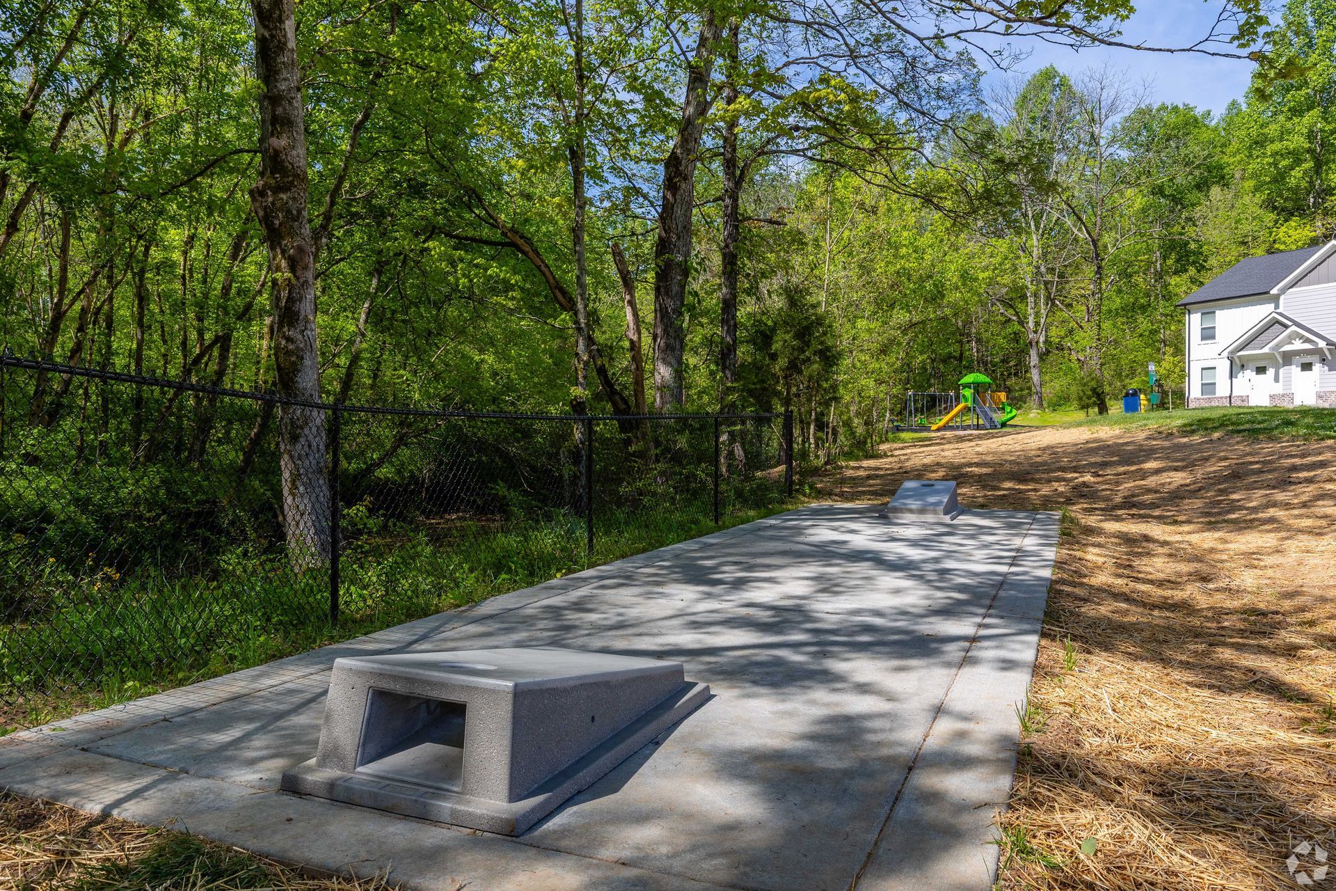 Concrete skate feature in a grassy area with trees and a playground in the background.