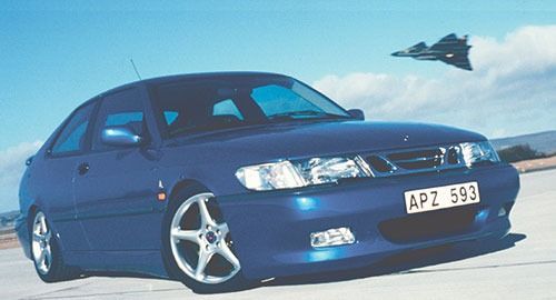Blue Saab 9-3 coupe with a fighter jet overhead, on a runway under a clear sky.