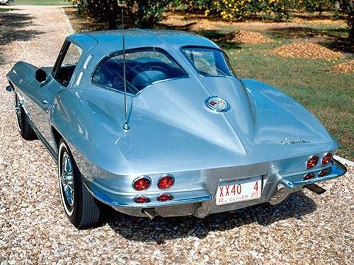 Silver 1963 Corvette Sting Ray coupe on gravel driveway, viewed from rear, antenna and taillights visible.