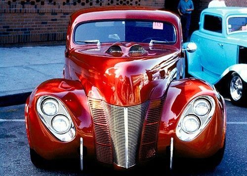Red custom hot rod with chrome grille and headlights, parked outdoors.