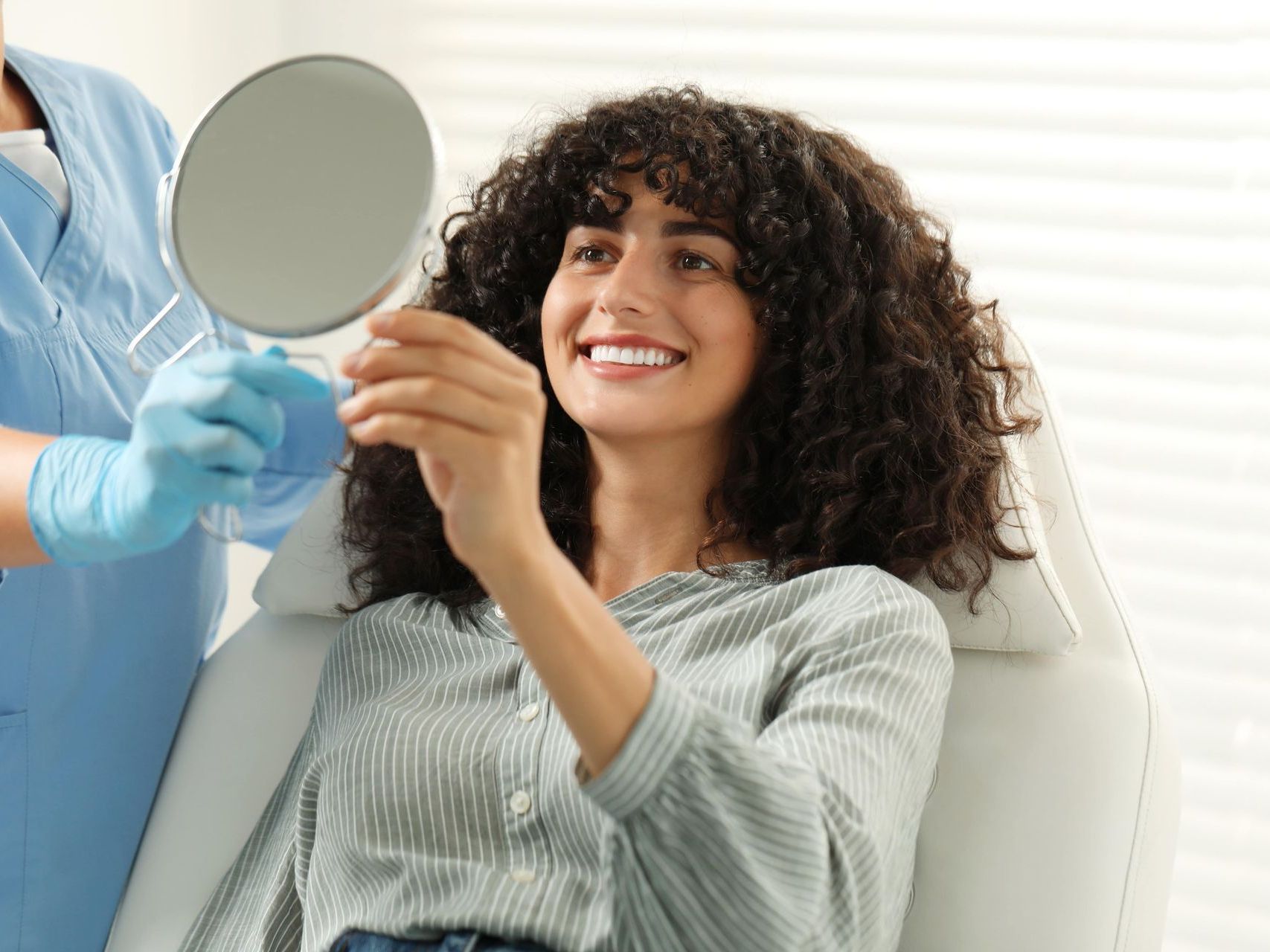 A woman is smiling while looking at her teeth in a mirror