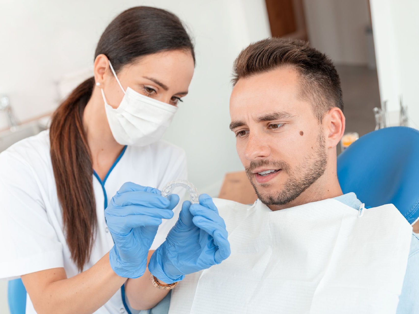 A man is sitting in a dental chair while a female dentist examines his teeth