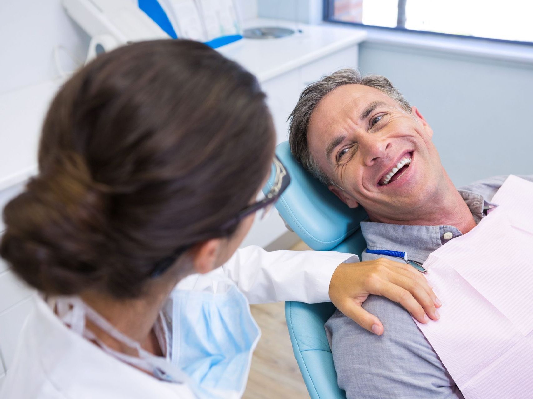 A man is sitting in a dental chair talking to a female dentist