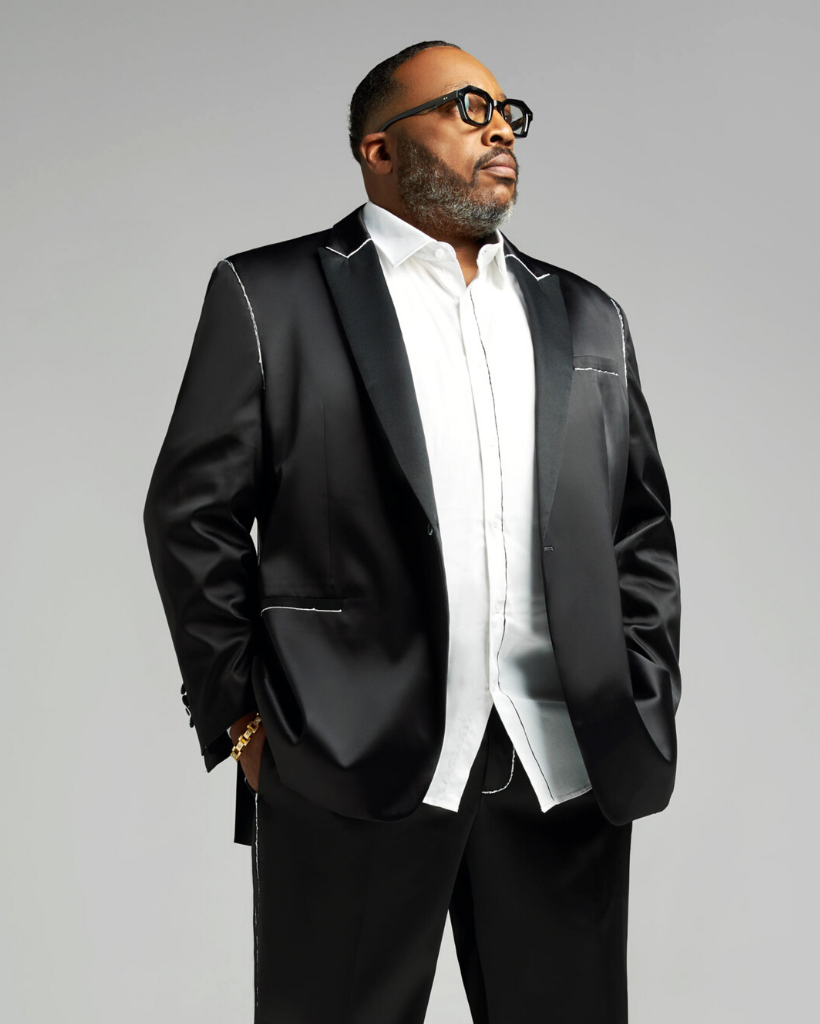 A man in a black suit and white shirt is standing with his hands in his pockets.