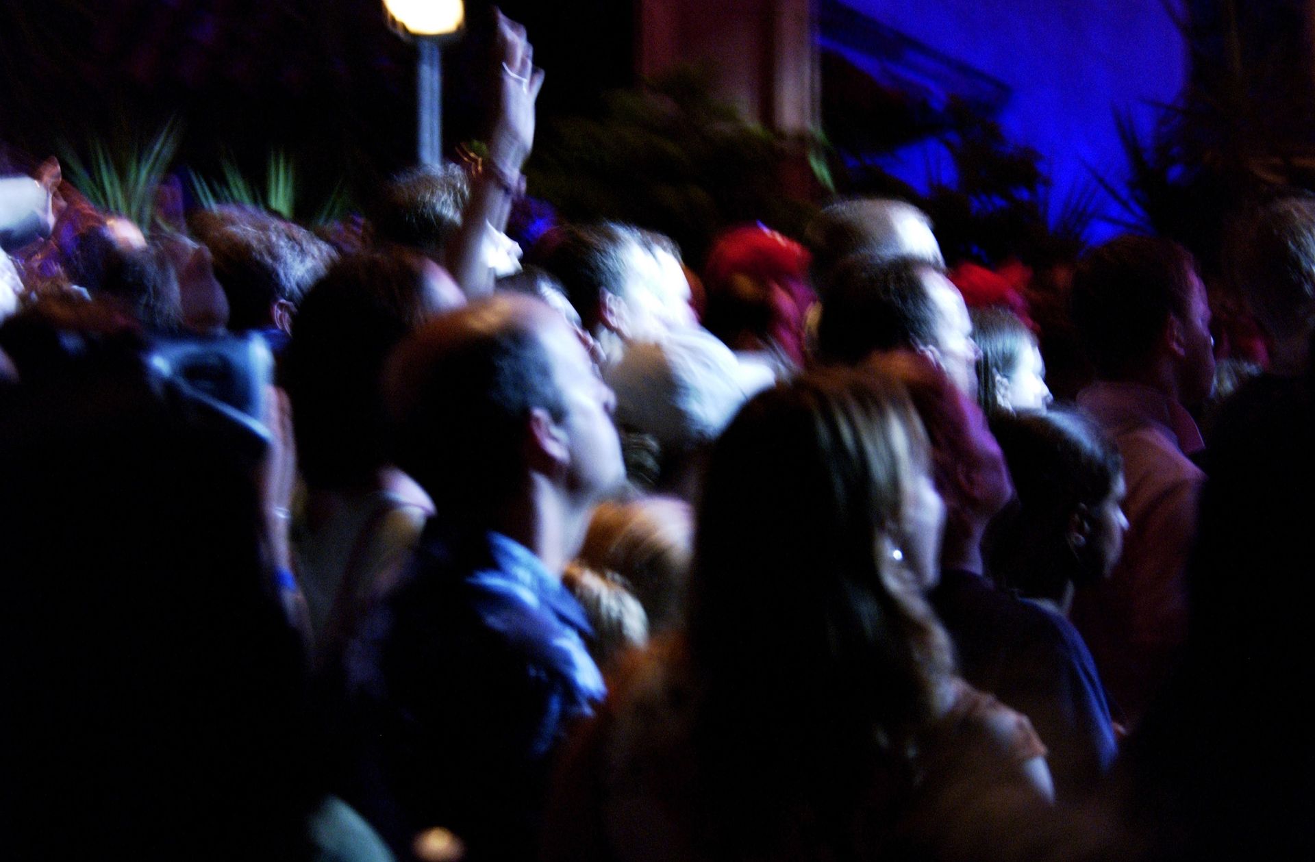 A crowd of people are standing in a dark room with their hands in the air.