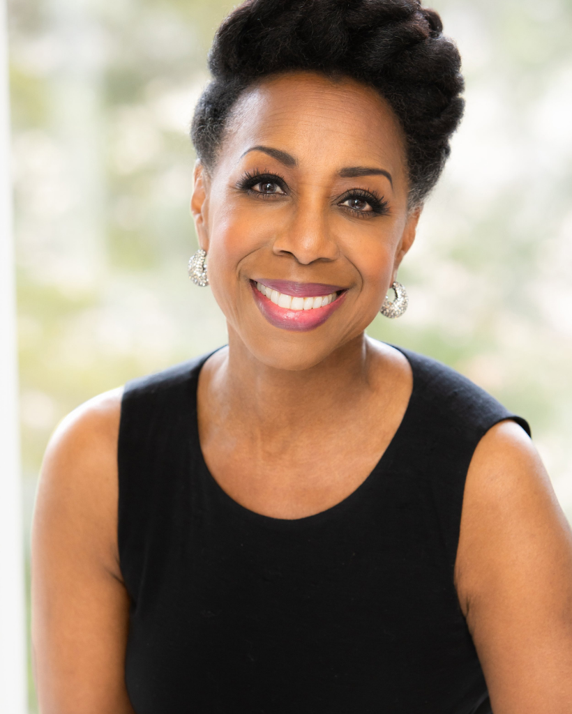 A woman wearing a black tank top and earrings is smiling for the camera.