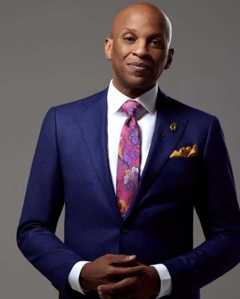 A man in a suit and tie is standing with his hands folded.