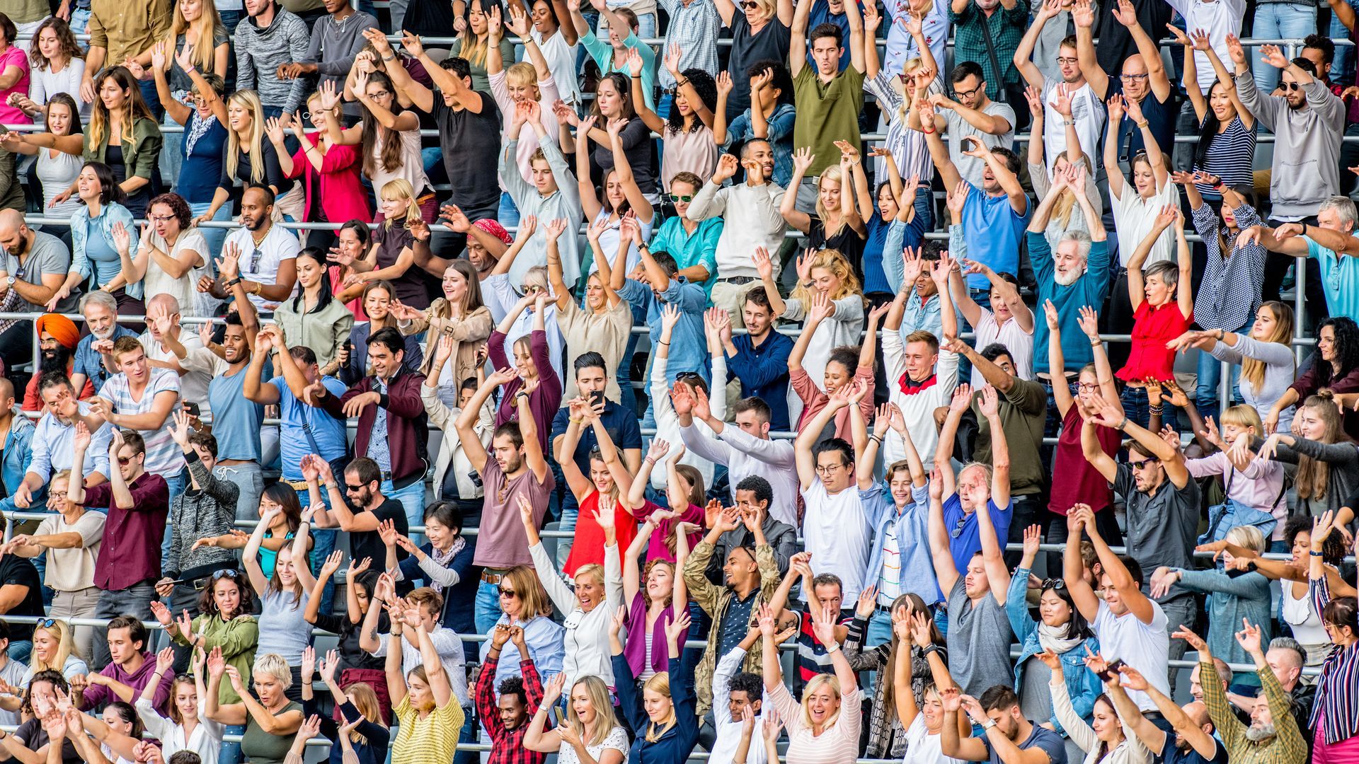 A large group of people are sitting in a stadium with their arms in the air.