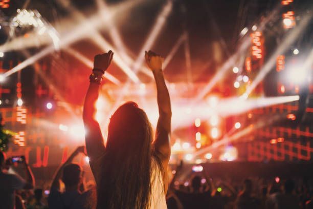A woman is standing in front of a crowd at a concert with her arms in the air.