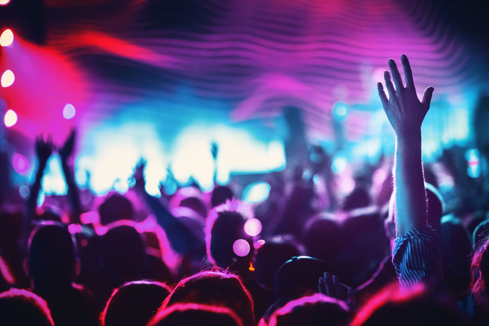 A crowd of people are dancing at a concert with their hands in the air.
