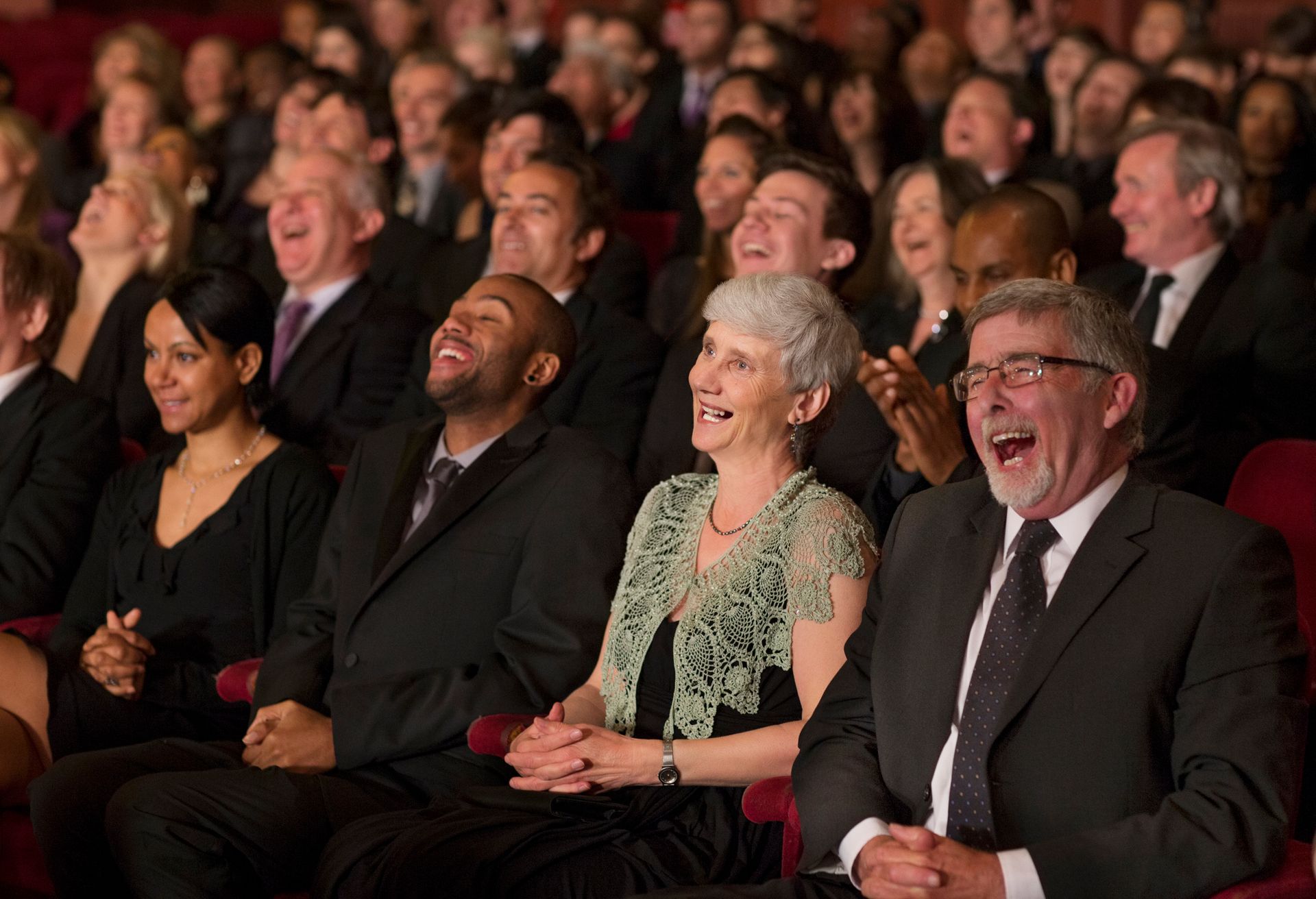 A large group of people are sitting in a theater laughing.