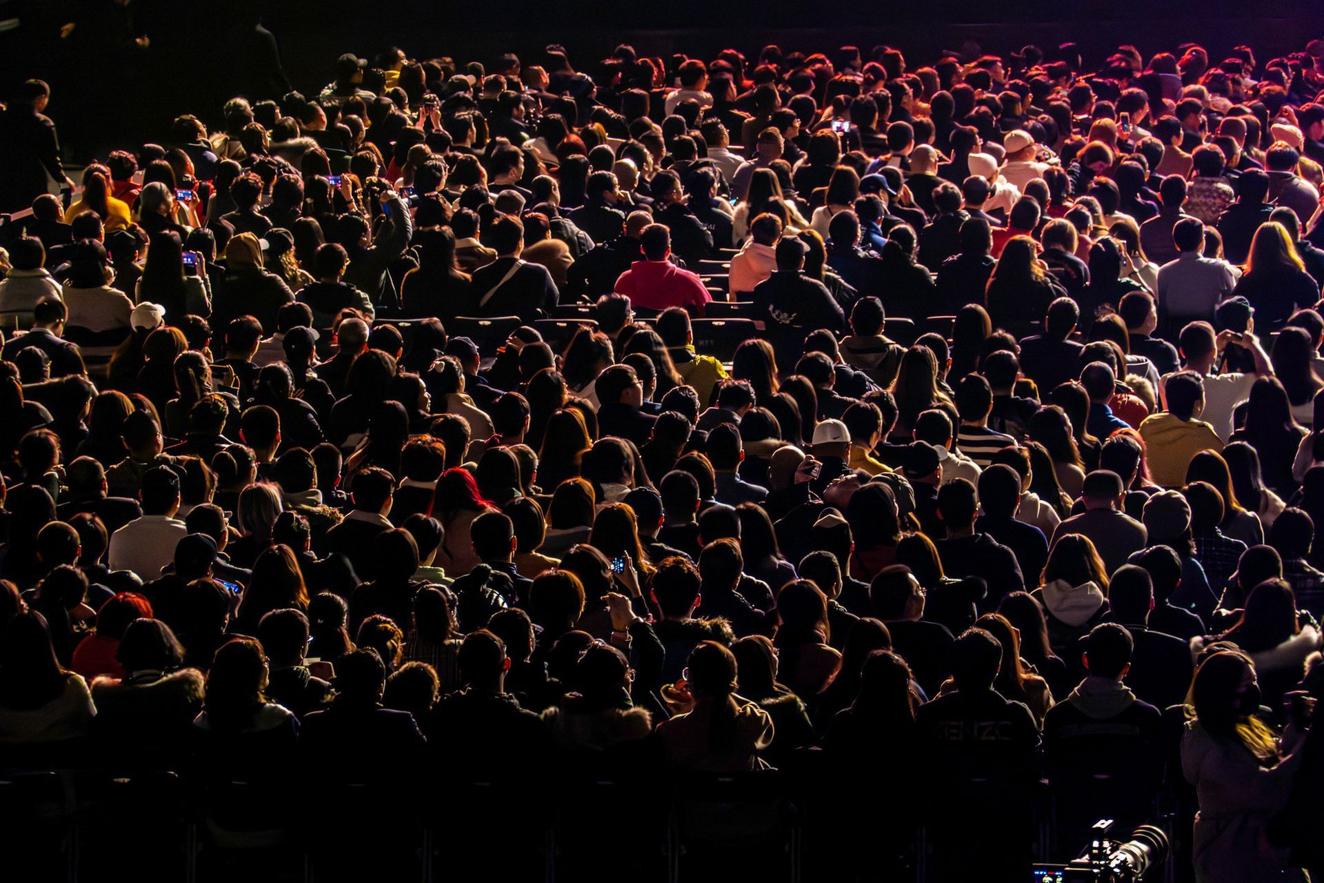 A large crowd of people are sitting in a dark room at a concert.
