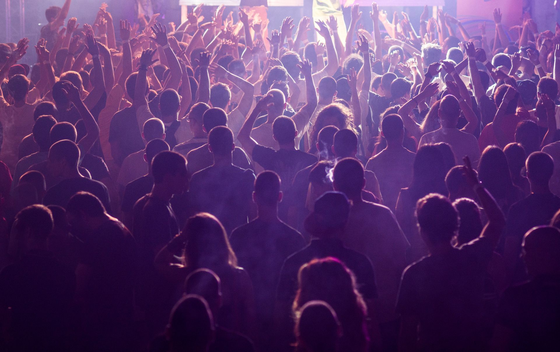 A crowd of people are dancing at a concert with their hands in the air.