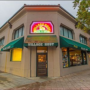 The front of a restaurant with green awnings and a neon sign.