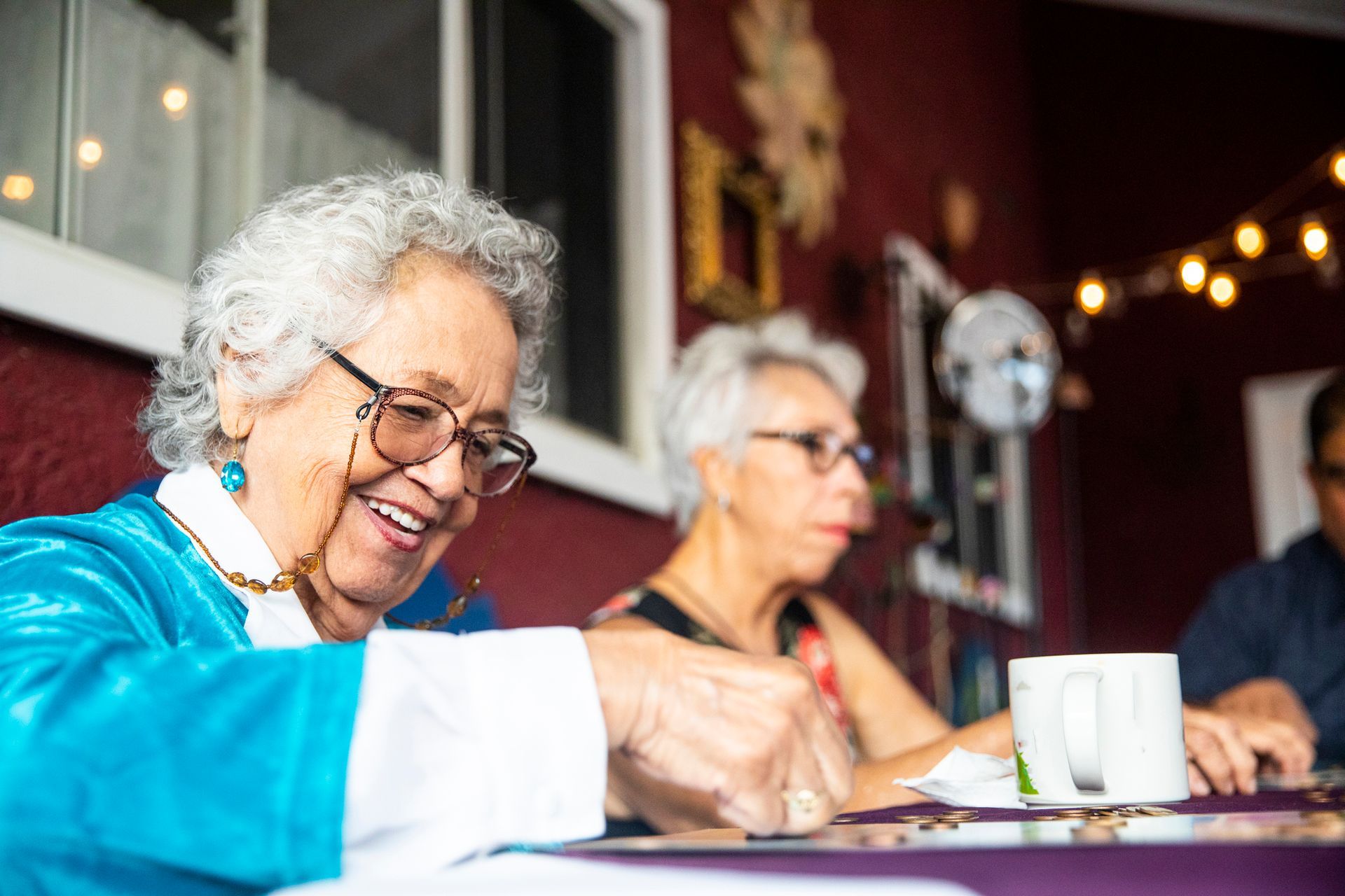 An elderly woman is sitting at a table playing a game of puzzles.