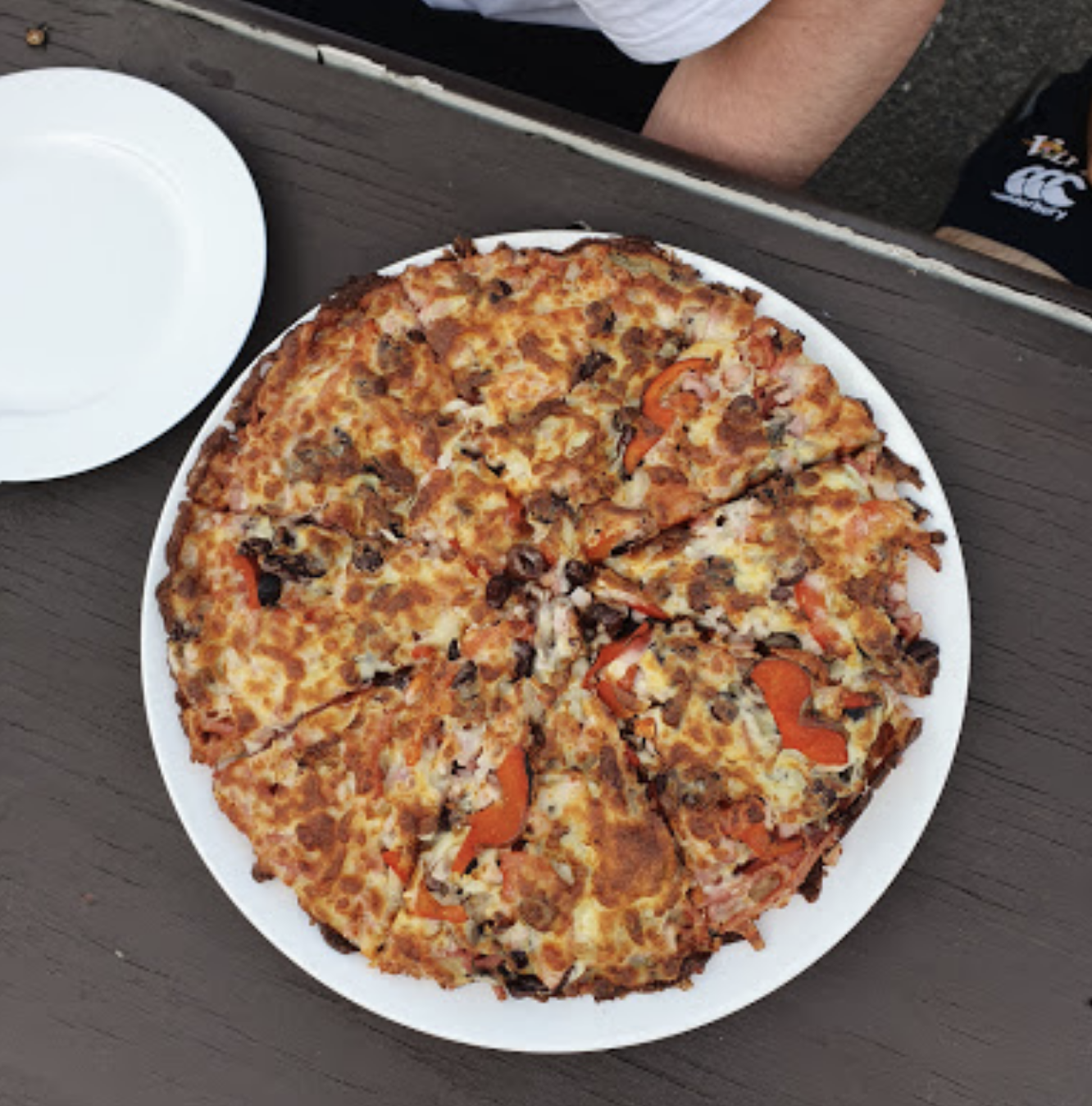 A pizza on a white plate next to a white plate — Bella M Pizzas in Bundaberg North, QLD