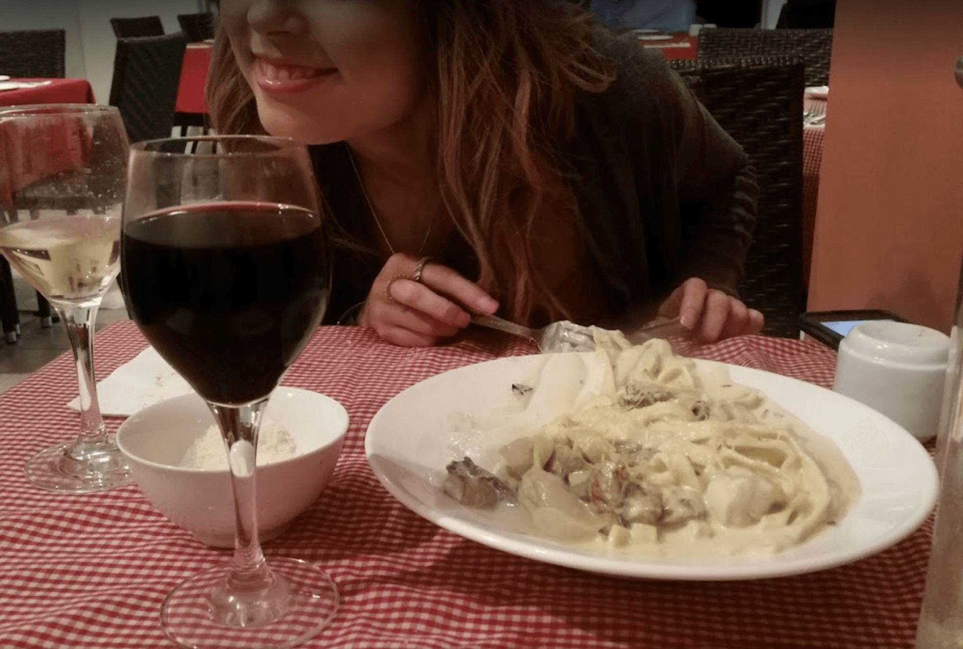 A woman is sitting at a table with a plate of pasta and a glass of wine — Bella M Pizzas in Bundaberg North, QLD