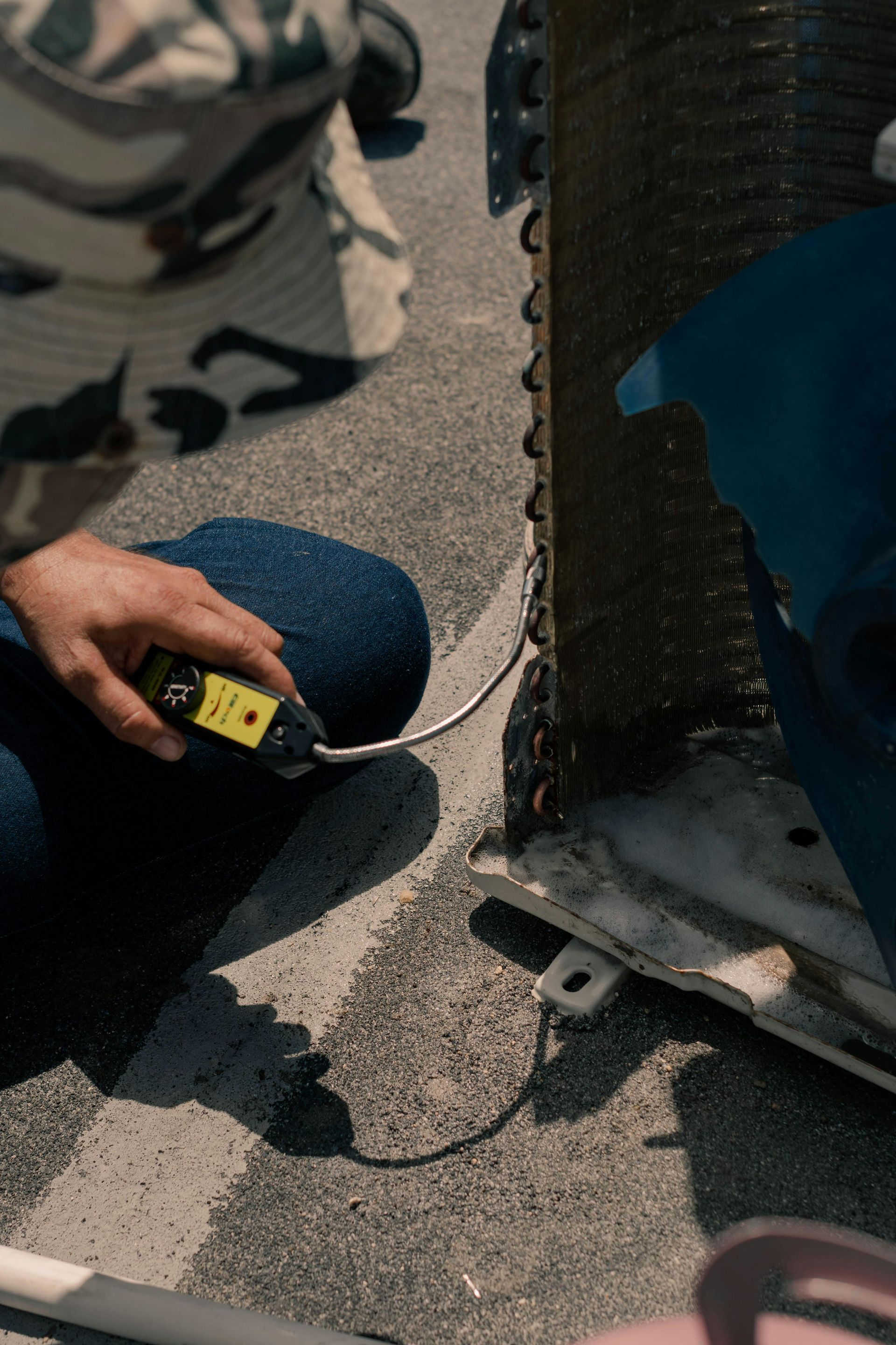 Person inspecting an air conditioner coil with a testing device on a rooftop.