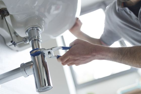 A man is fixing a sink with a wrench.