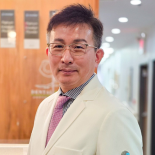 Man in a white suit and pink tie standing in a bright office hallway, facing the camera.