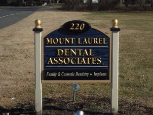 A roadside sign for Mount Laurel Dental Associates at 220, featuring gold lettering on a dark blue background.