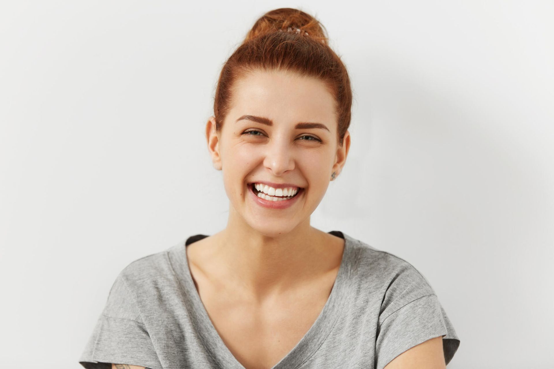 A woman is smiling with her eyes closed and her hair in a bun.