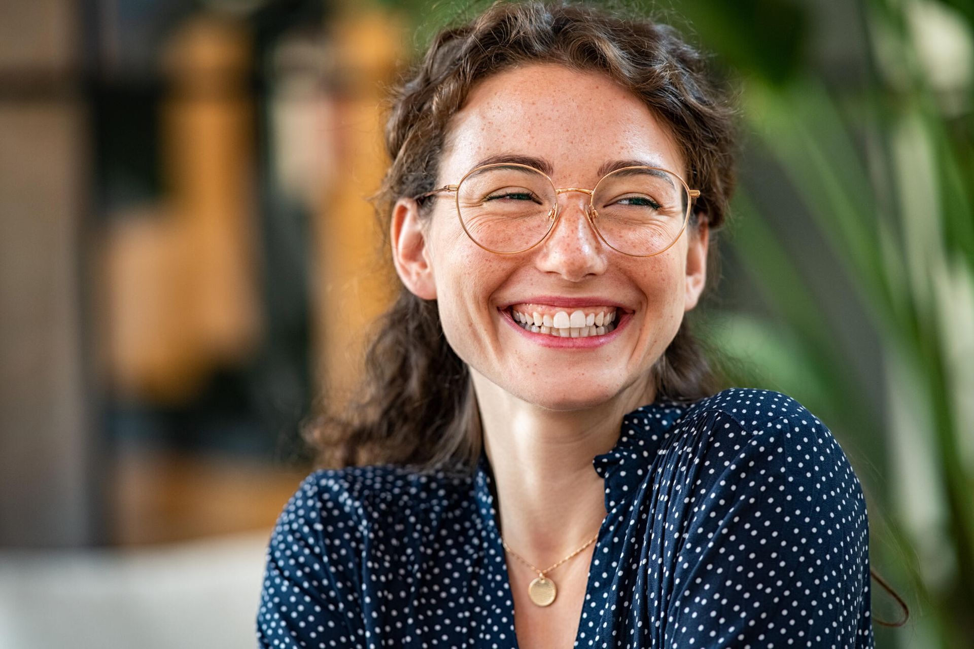 A woman wearing glasses and a polka dot shirt is smiling.