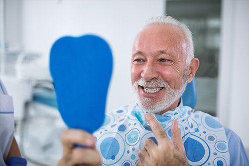 senior man smiling in mirror while sitting in dental chair