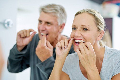Middle-aged couple flossing in mirror
