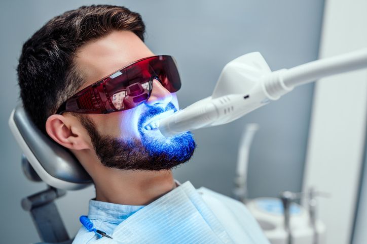 Patient wearing red goggles receiving blue light teeth whitening in a dental chair