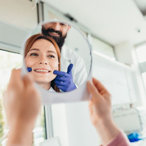 Dentist checking a smiling patient’s teeth in a mirror during a dental exam