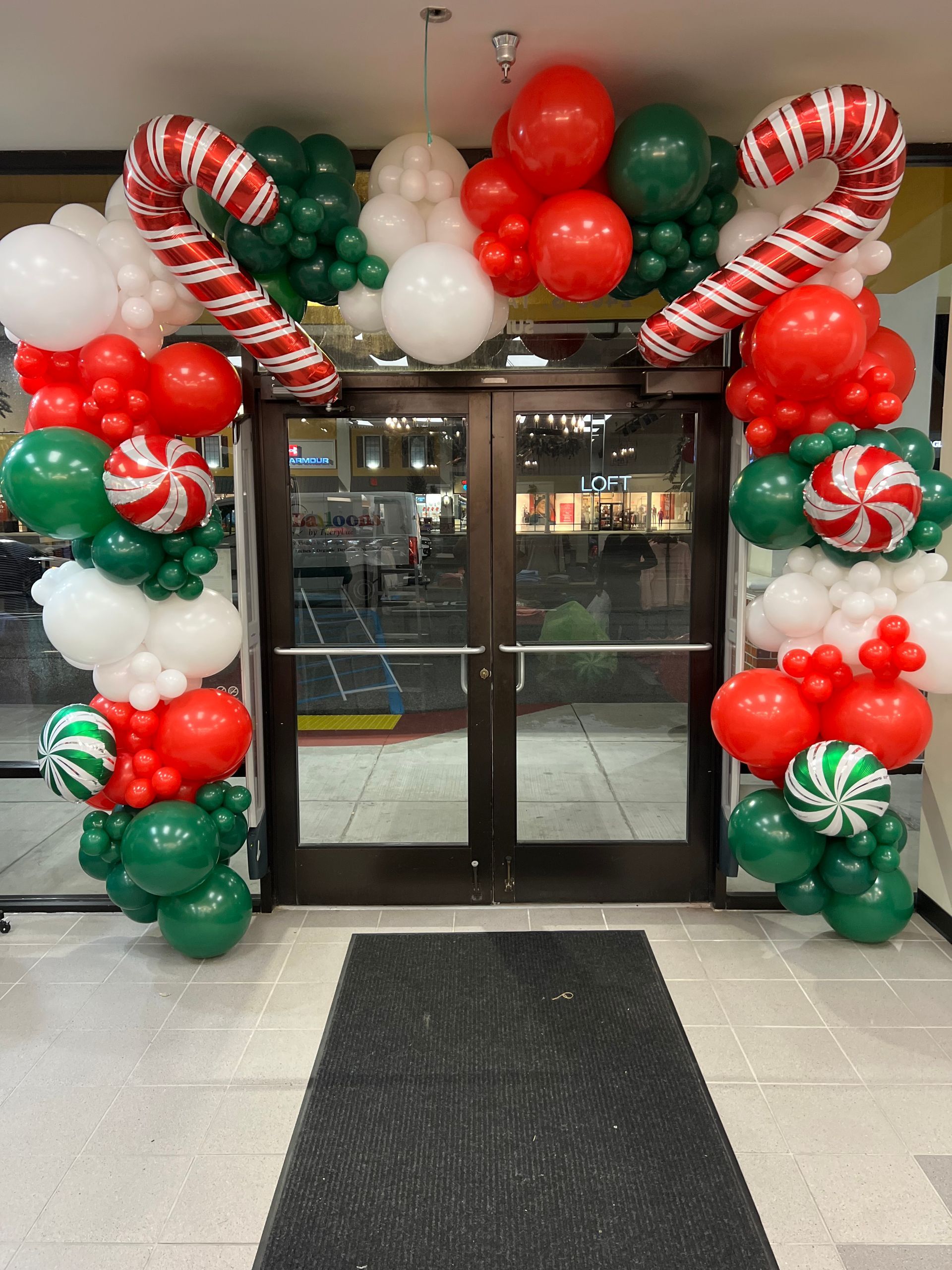 A doorway decorated with red , green and white balloons and candy canes.