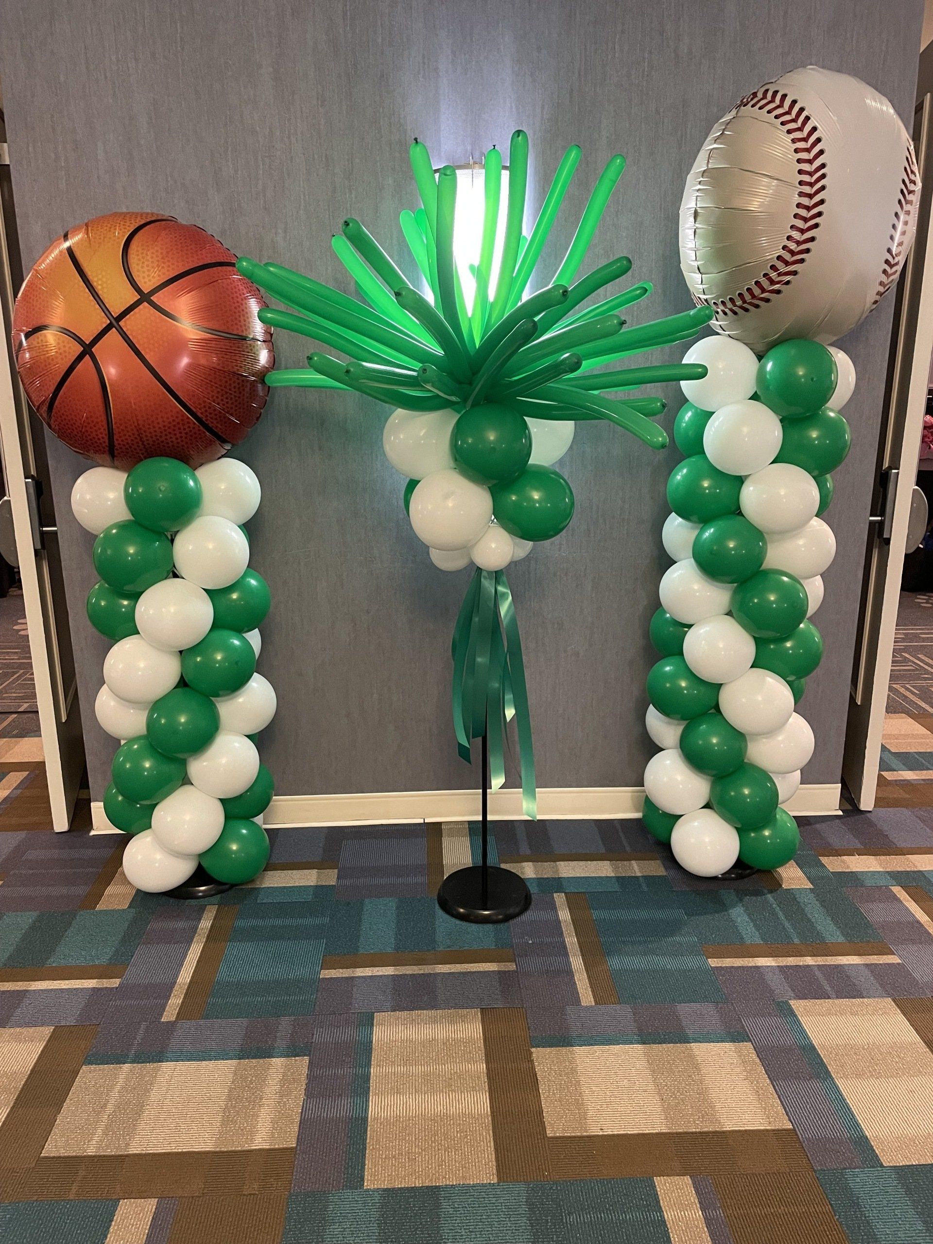 A basketball and a baseball are sitting on top of green and white balloons.