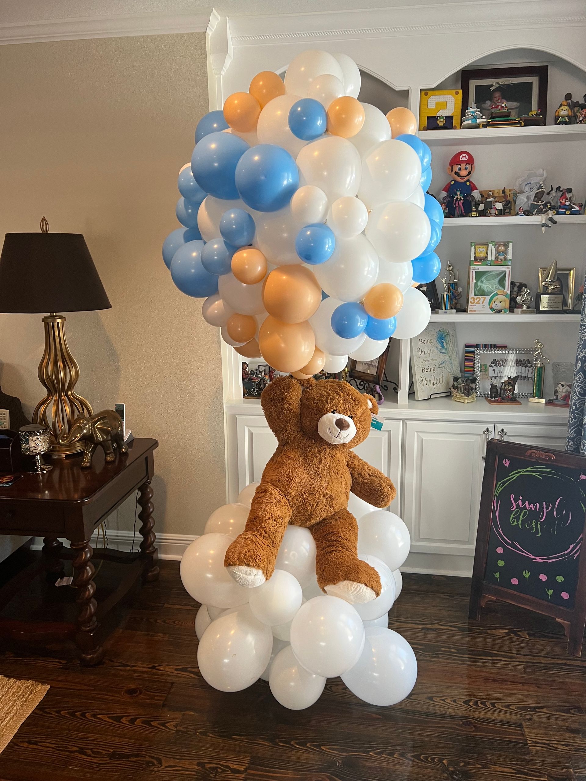 A teddy bear is sitting on top of a bunch of balloons in a living room.