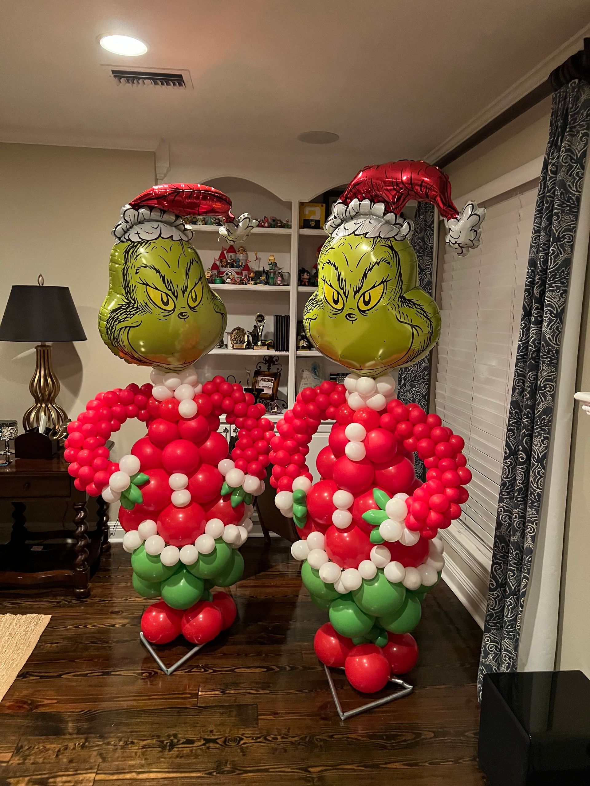 Two grinch balloons are standing next to each other on a wooden floor in a living room.
