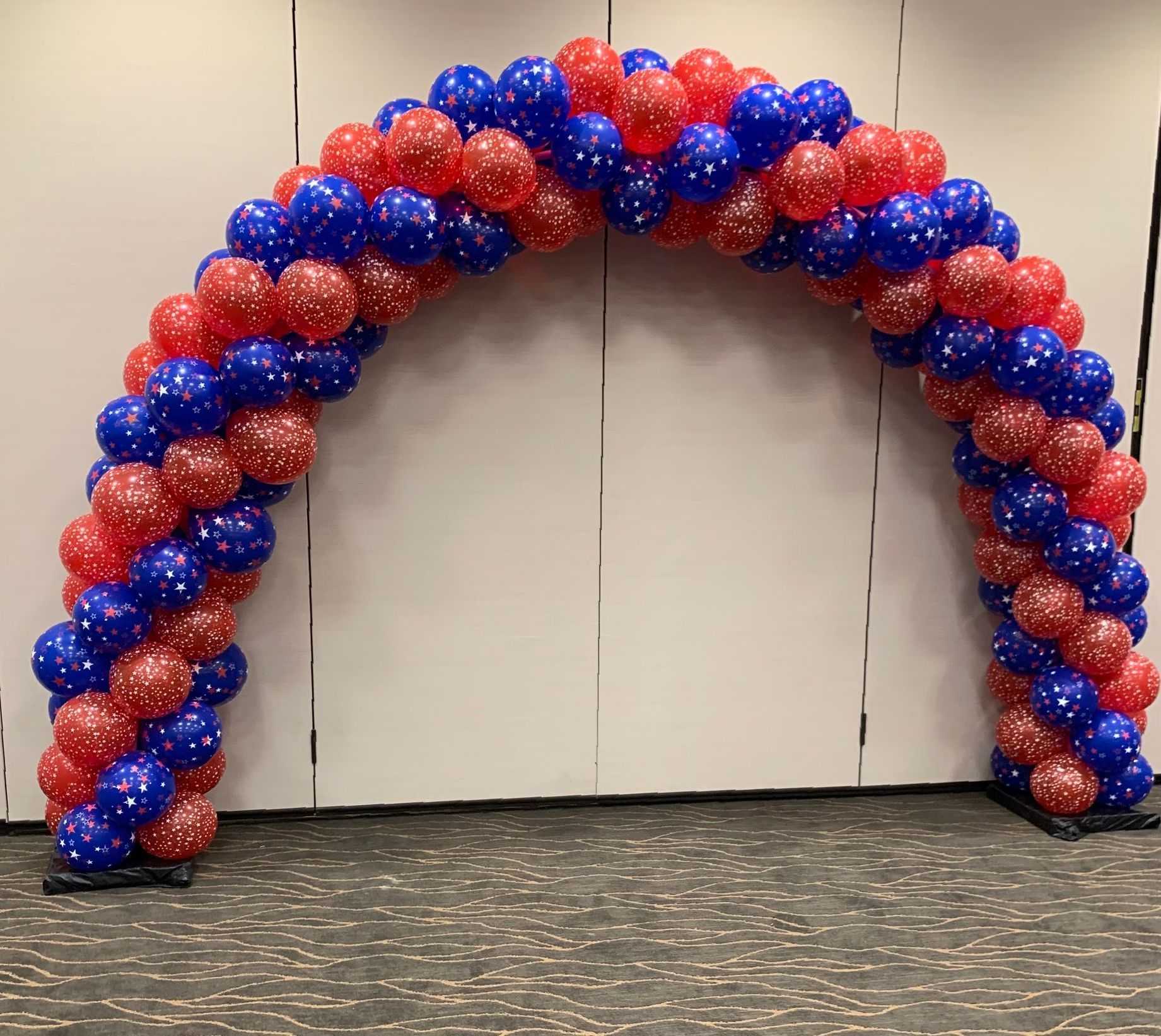 A red and blue balloon arch is sitting in front of a white wall.