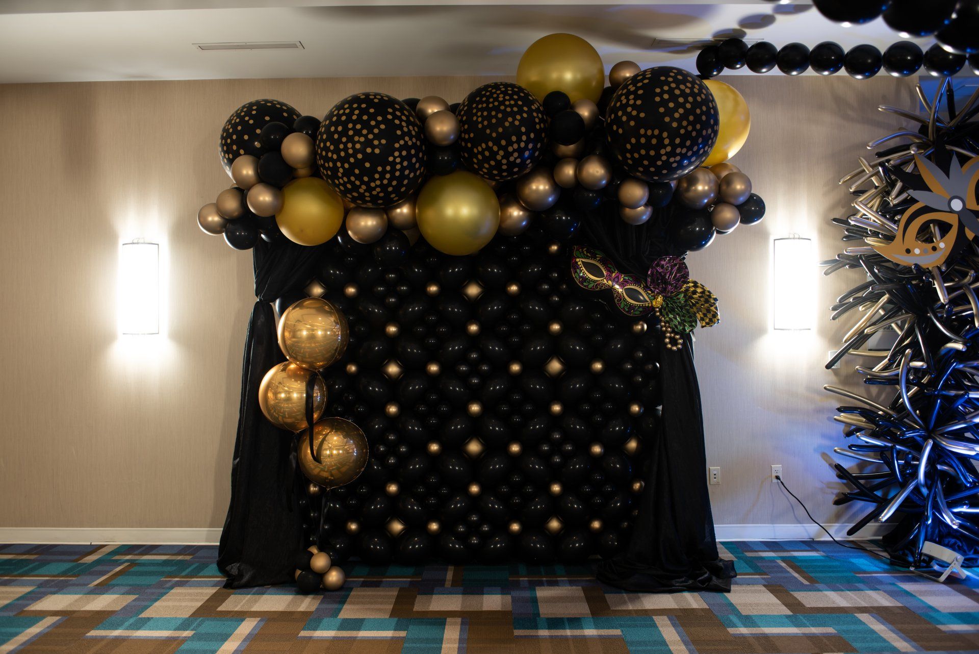 A wall of black and gold balloons in a room.