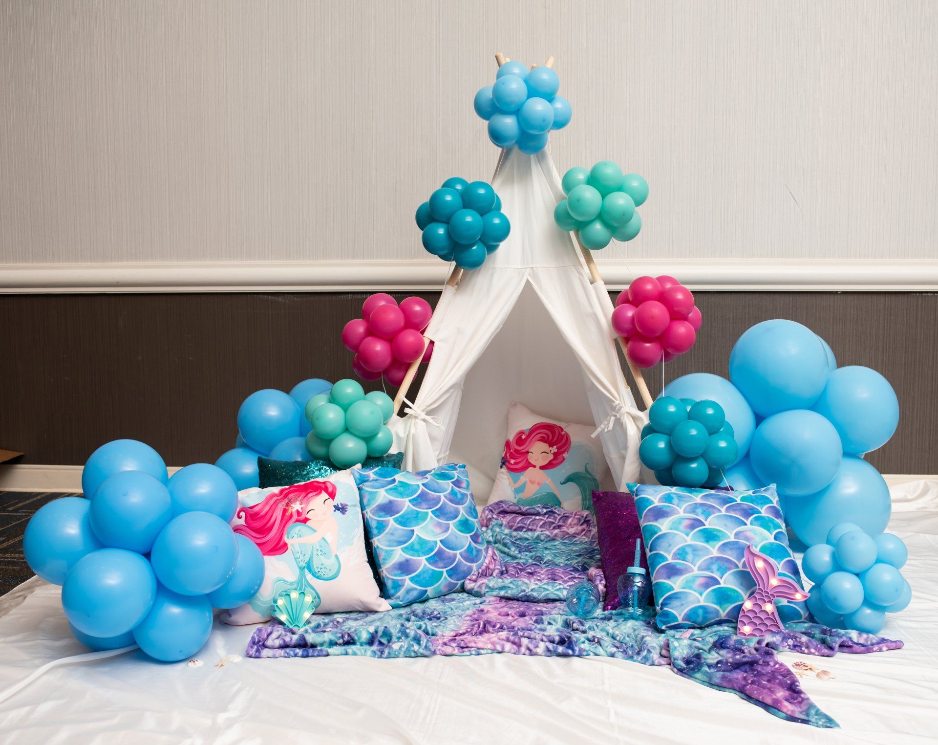 A mermaid themed teepee with balloons and pillows on a bed.