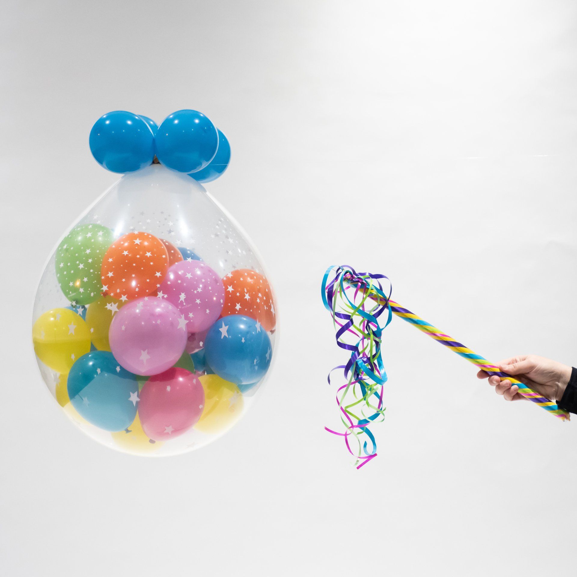 A person is holding a wand next to a balloon filled with balloons.