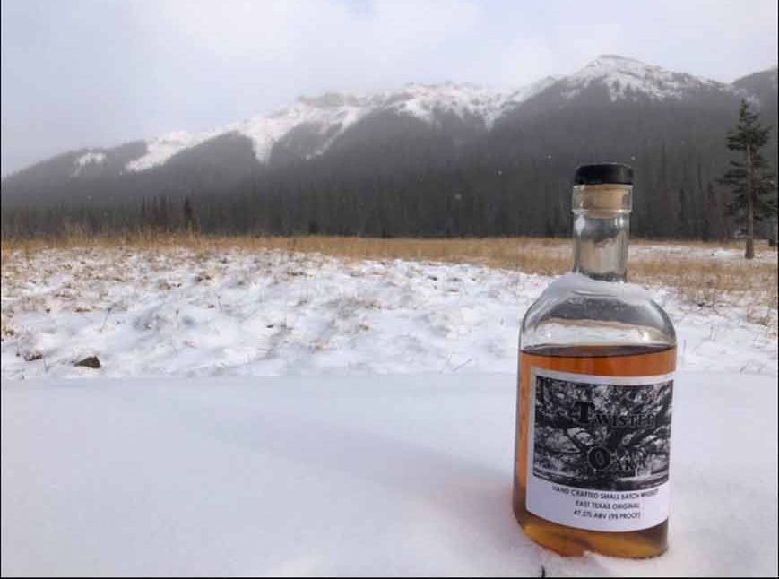 A bottle of alcohol is sitting in the snow with a mountain in the background.