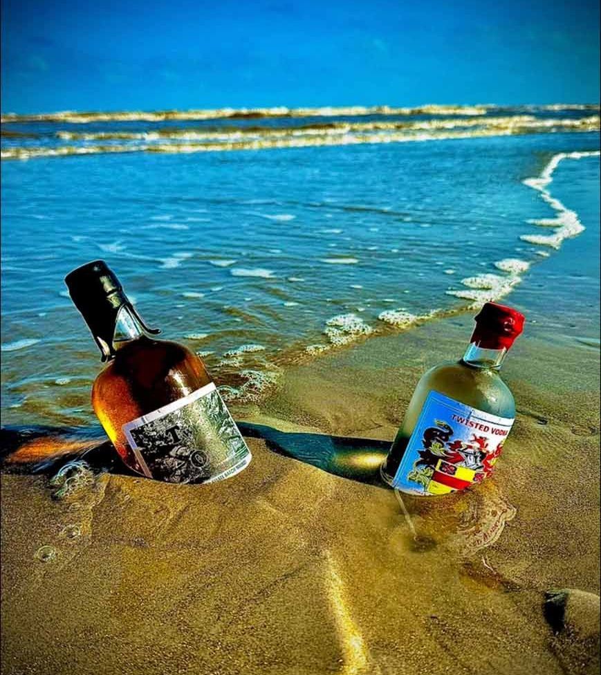 Two bottles of alcohol are sitting in the sand on the beach.
