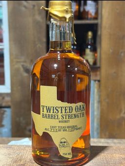 A bottle of twisted oak barrel strength whiskey is sitting on a wooden table.