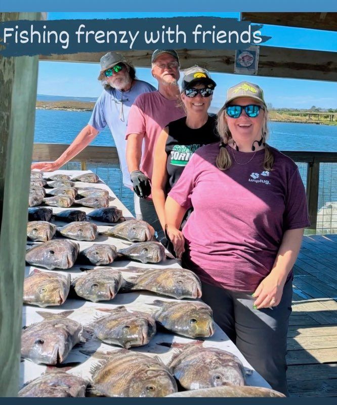 Four people stand behind a table covered in fish, on a pier with water in the background.