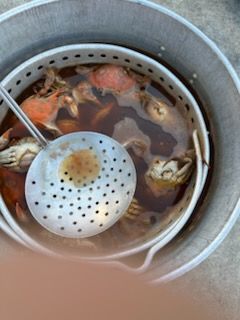 Crabs cooking in a metal pot with a slotted spoon.