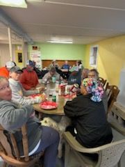 People at a table inside, eating and talking. One person has a dog.